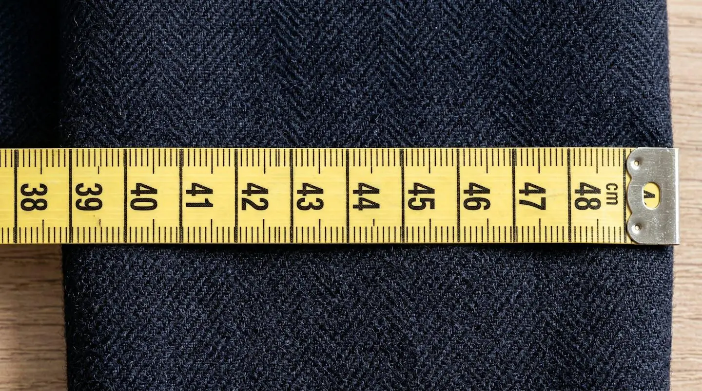 Vue en gros plan d'un mètre ruban de tailleur posé sur un tissu de costume haut de gamme, texture visible et lumière naturelle